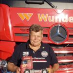 Detlef steht vor einem Lkw und hält in den Händen eine kleine Nachbildung des Lkw
